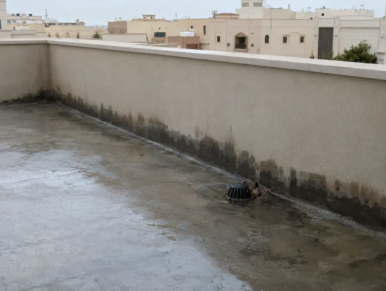 برك مطر وبقع رطوبة داكنة عند أسفل سور السطح بجانب فتحة تصريف
